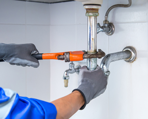 plumbing engineer using wrench to repair water pipe under sink